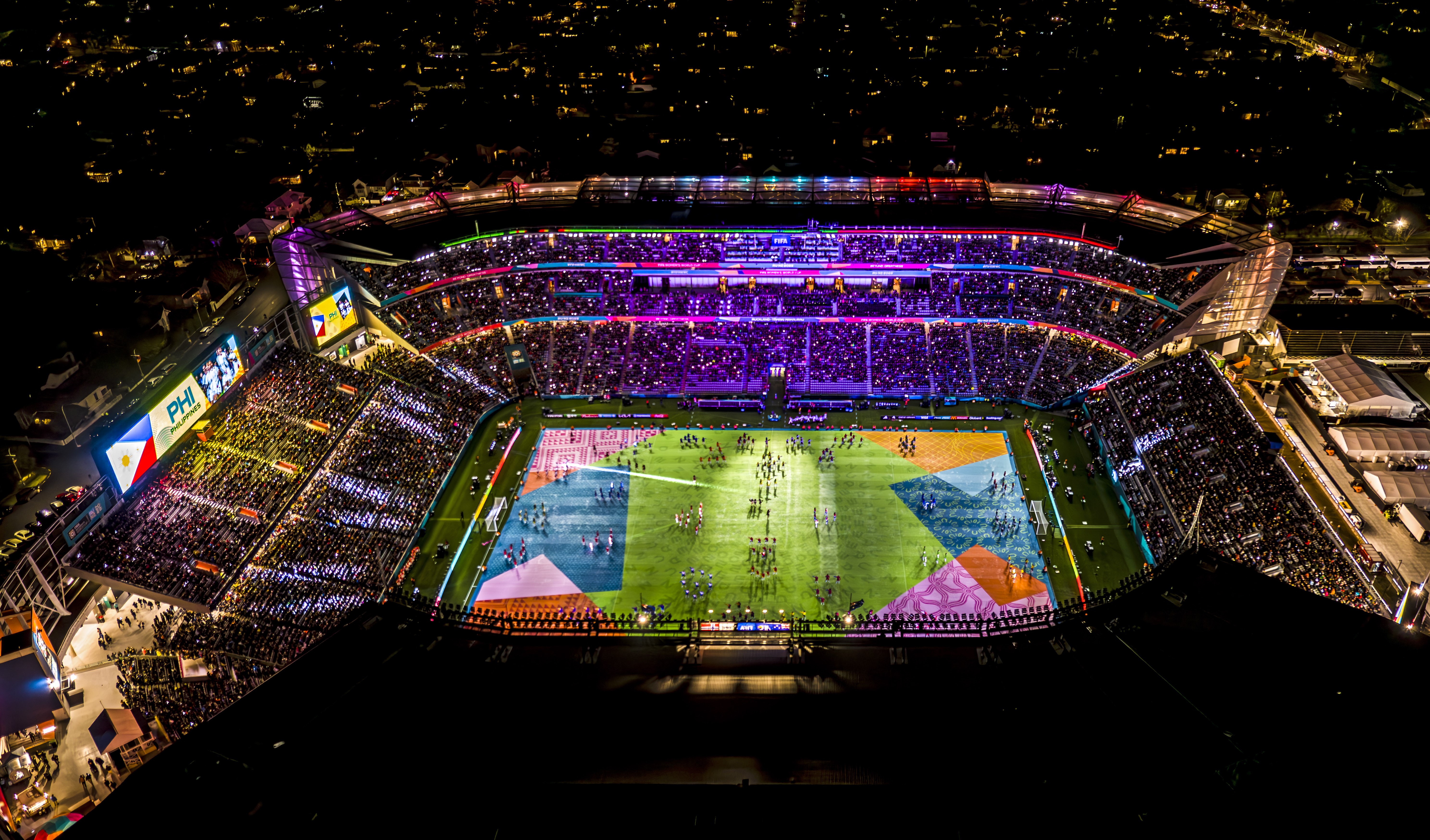 Eden park stadium at night lit up with different coloured lights.